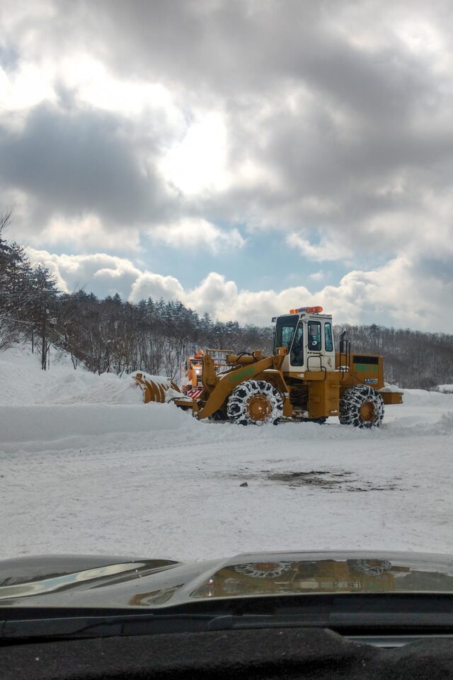 満車になった駐車場を広げるため、せっせと除雪車で駐車スペースを広げている様子を先頭で眺めていました。我々の後ろには同じく駐車場待ちの車がずらーー。